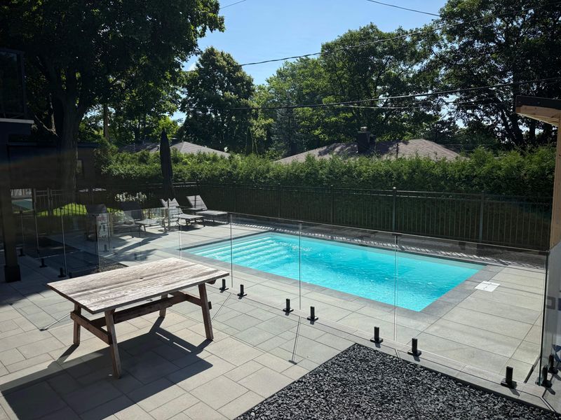 Cour arrière avec piscine, dalles de pavé et garde-corps de verre réalisés par Vallières Paysagiste